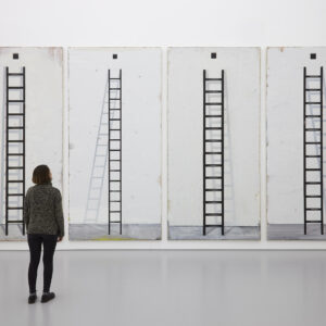 A visitor stands looking at four tall paintings of ladders. Each painting has a shadow appearing differently behind the ladder.