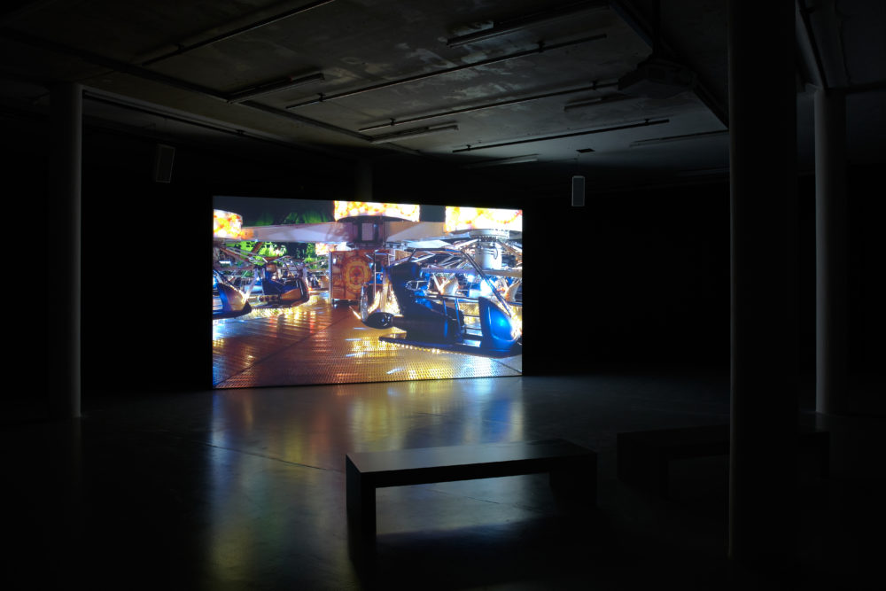 Installation view of Anna Franceschini THE PLAYER MAY NOT CHANGE HIS POSITION (2009). A projection of a fairground shows in a dimly lit gallery.