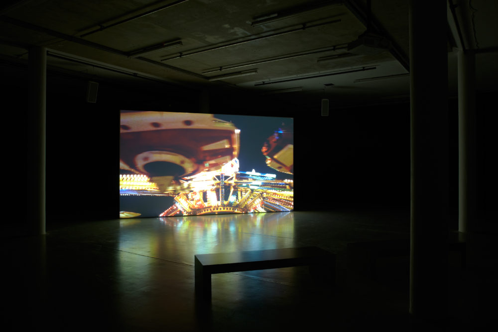 Installation view of Anna Franceschini THE PLAYER MAY NOT CHANGE HIS POSITION (2009). A projection of a fairground shows in a dimly lit gallery.