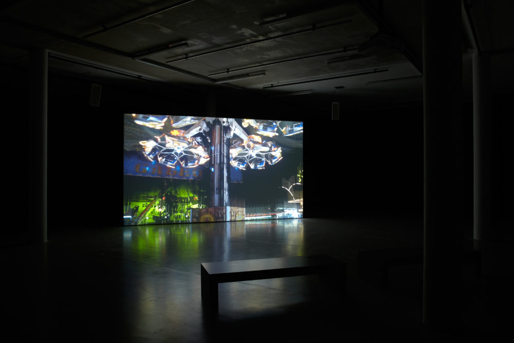 Installation view of Anna Franceschini THE PLAYER MAY NOT CHANGE HIS POSITION (2009). A projection of a fairground shows in a dimly lit gallery.