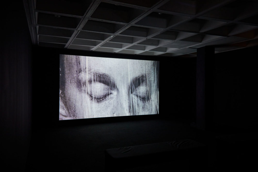 A piece from Basin Magdy, The Stars Were Aligned for a Century of New Beginnings (2017) at Arnolfini. A projection of a man's face as water pours down it.