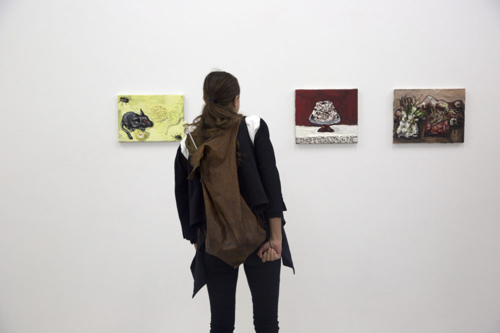 Installation view of Bloomberg New Contemporaries (2013) A visitor studies small canvas paintings hung on a wall.
