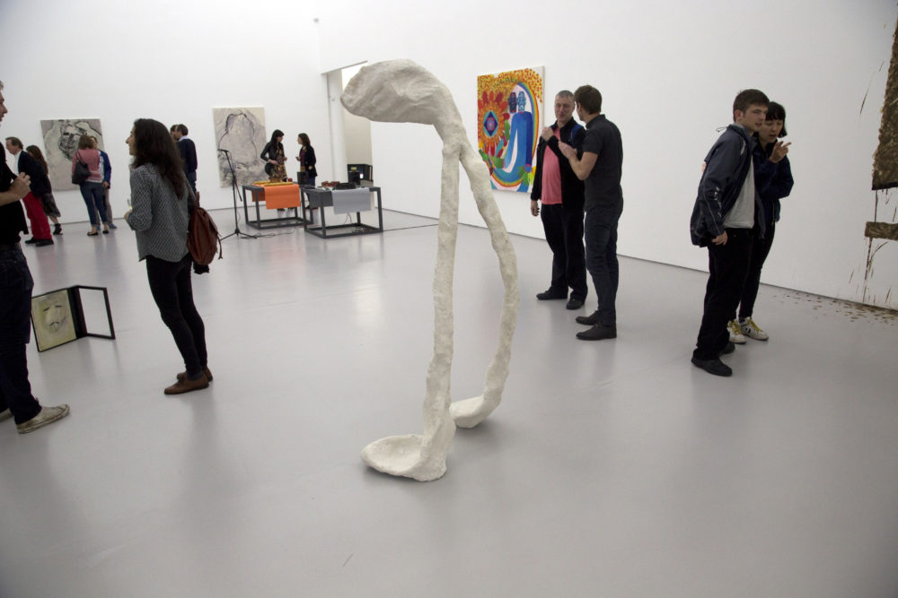 Installation view of Bloomberg New Contemporaries (2013) Visitors interact with the works. In the foreground is a large sculpture in the shape of a wishbone.
