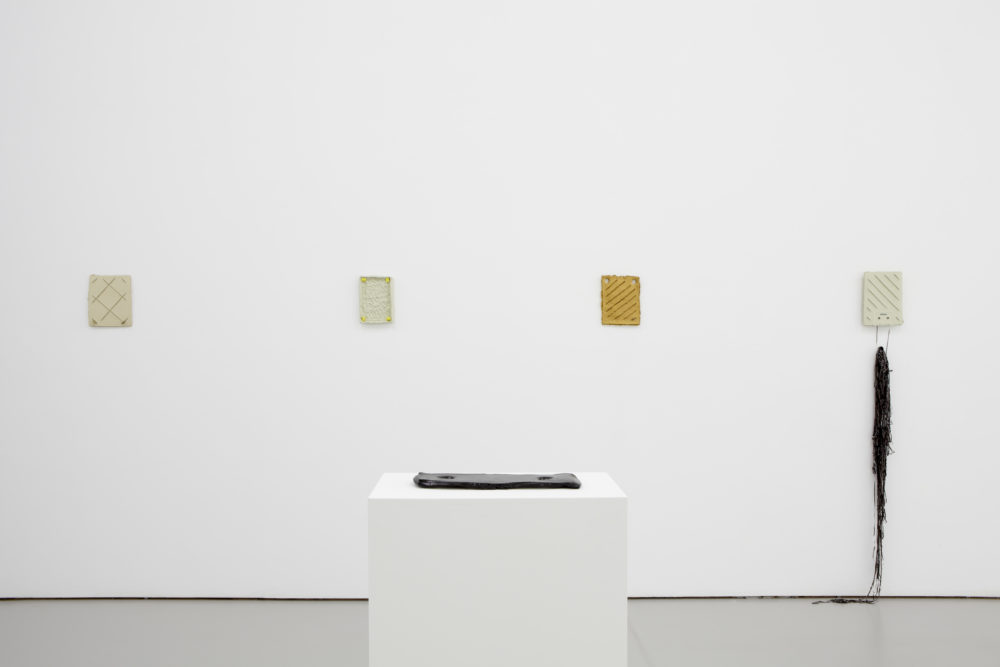 Installation view of Bloomberg New Contemporaries (2013). A series of flat, rectangular sculptures hang in the gallery, one sits on a plinth.