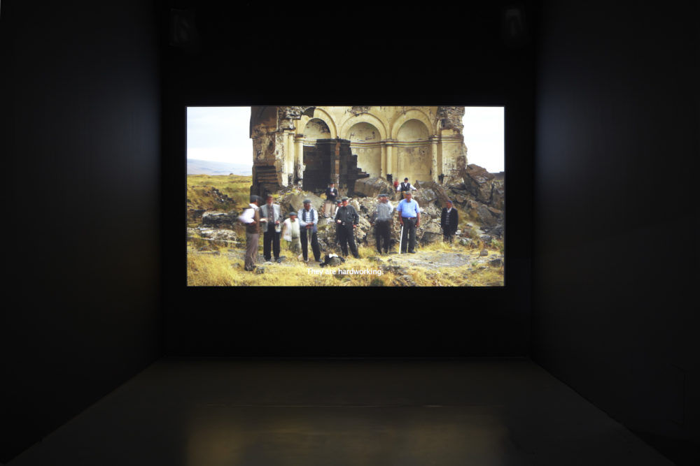 Installation view of Bloomberg New Contemporaries (2013). A projection of a group of men next to some ruins is subtitled 