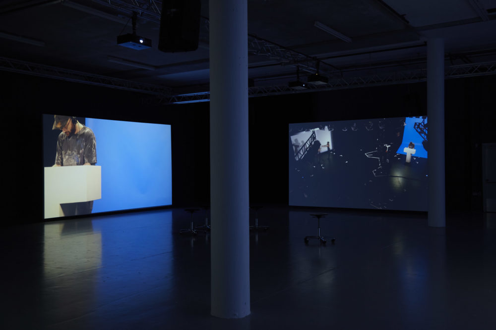 Two screens are in the gallery - each shows a show runner at a plinth on a set similar to a gameshow's set.