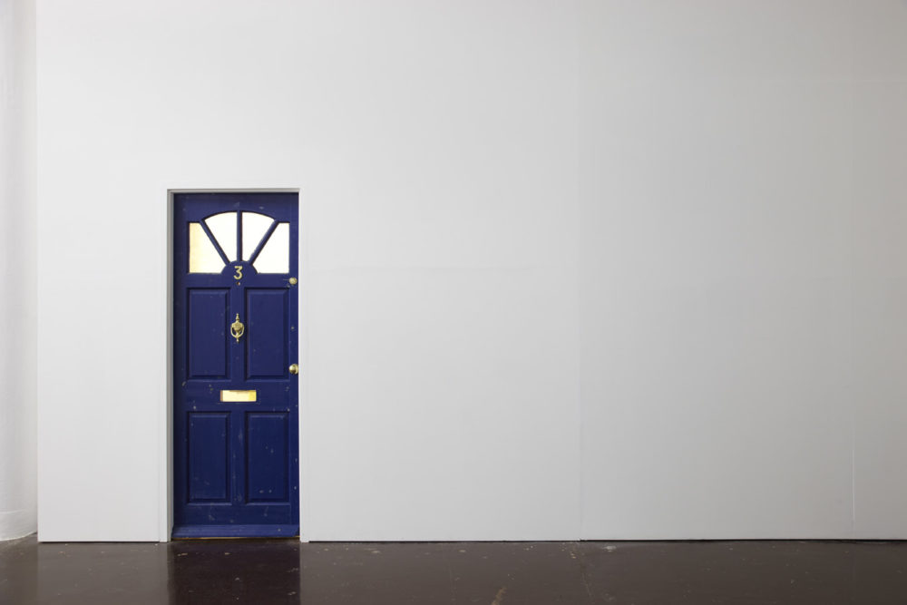 Installation view of Cezary Bodzianowski, Tea Back (2011). The gallery is light. A wooden front door for a house is built into the gallery wall.