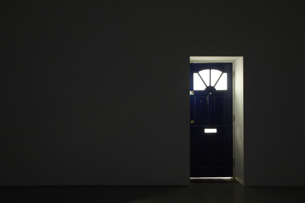 Installation view of Cezary Bodzianowski, Tea Back (2011). The gallery is very dark - a wooden front door for a house is built into the gallery wall and light pours from behind it.