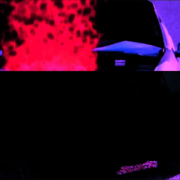 Film still: A large black rectangle obscures most of the image. Behind the rectangle it looks as though a car is on fire.