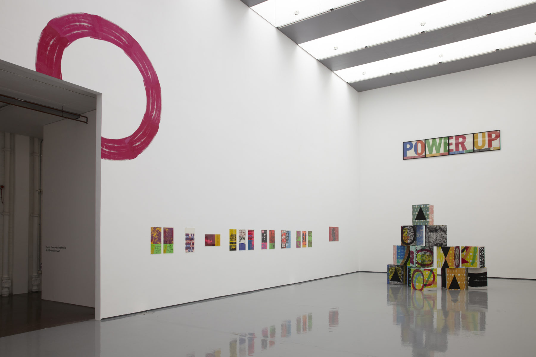 Installation view of Ciara Phillips and Corita Kent, Pull Everything Out (2012) A pyramid of multi coloured large cubes sits in the gallery. Screen prints hang on the wall.