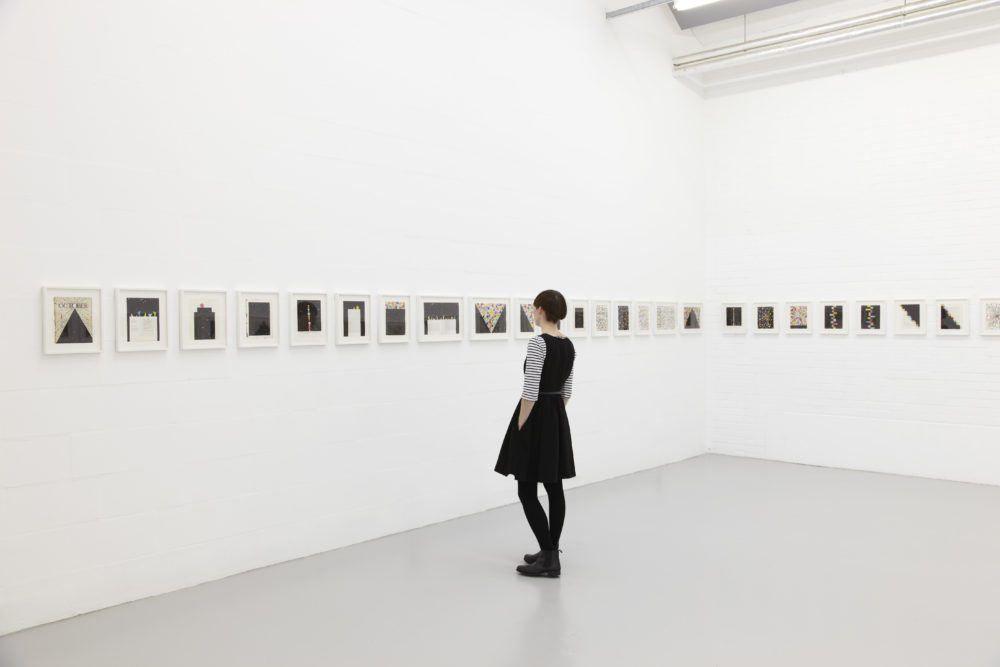 Installation view of David Batchelor Flatlands (2013). A visitor looks at several small works in white frames.