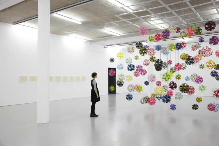 Installation view of David Batchelor Flatlands (2013). A visitor looks at plastic balls suspended from the ceiling.