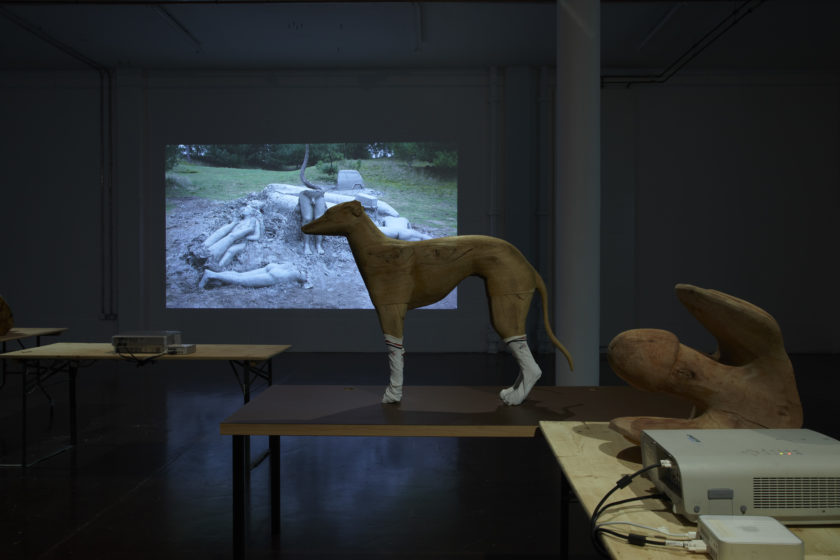 Installation view of Crêpe Suzette, (2012). A wooden carving of a whippet stands on a table and is wearing white sports socks.