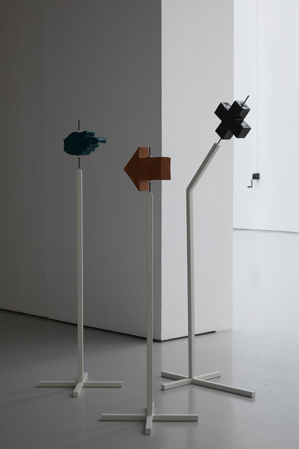 Metal stands hold up ceramic sculptures of a finger pointing right, an arrow pointing left, and a cross. These are placed at the gallery entrance.