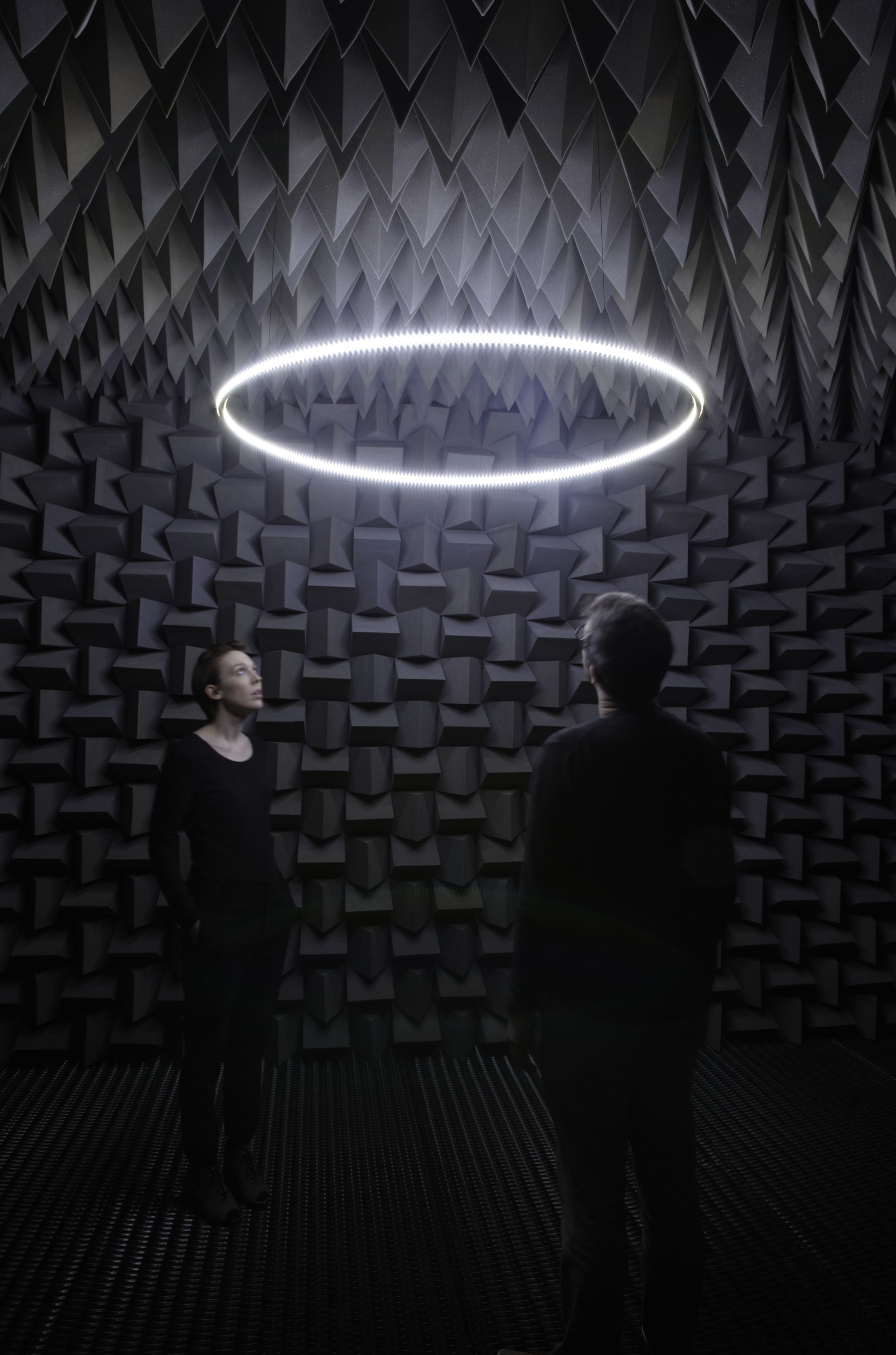 Installation view of Haroon Mirza. A ring of light is suspended in between walls covered in black sound proofing foam.