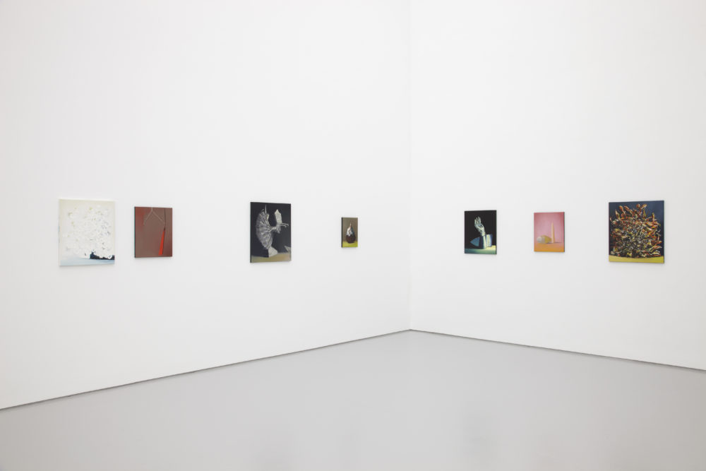 Installation shot: Seven unframed paintings hang on white walls.