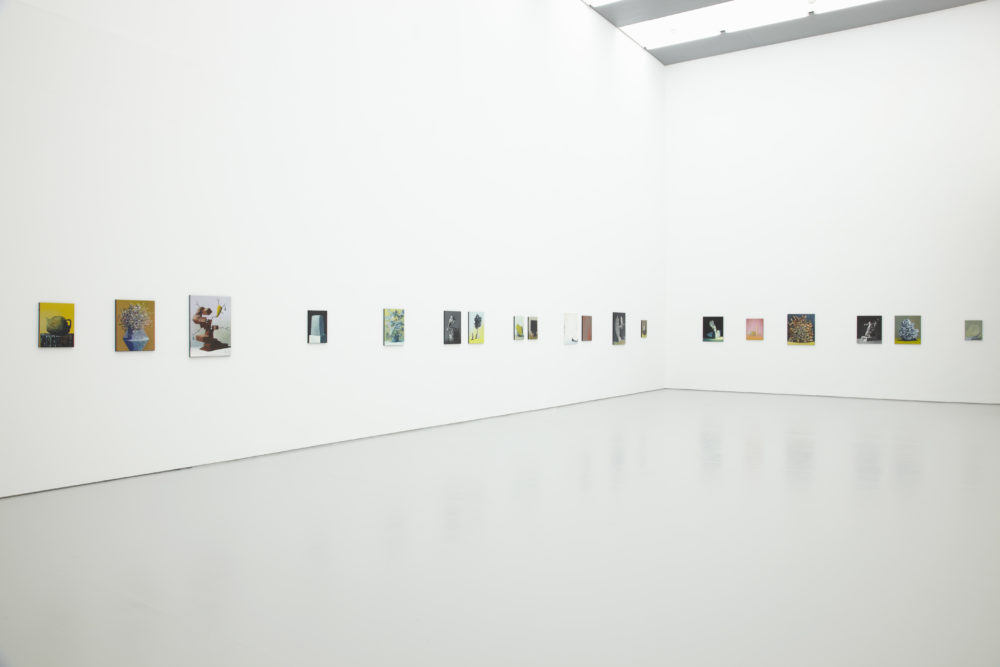 Installation shot: Nineteen unframed paintings hang on white walls.
