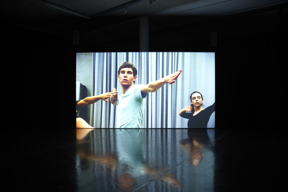 Installation view of Jesse Jones The Struggle Against Ourselves (2012). A projection of three people stretching their arms.