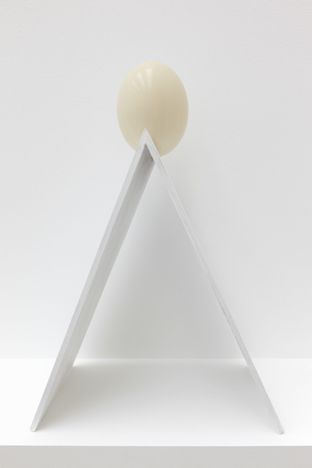 Installation view of Jessica Warboys Ab Ovo (2013). A white 'A frame' piece of wood is topped with a cream coloured egg.