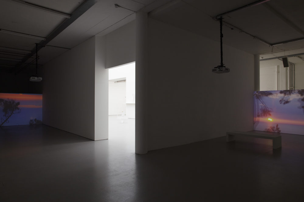 Installation view of Jessica Warboys, Ab Ovo (2013). The gallery is dimly light, a projection of a tropical night sky scene shows.