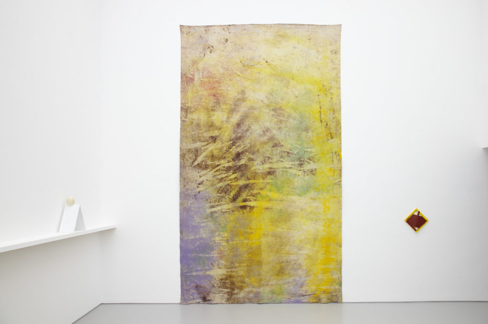 Installation view of Jessica Warboys Ab Ovo (2013). A large multi pastel coloured textile hangs on the gallery wall.