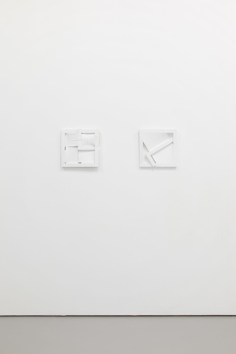 Installation view of Jessica Warboys, Ab Ovo (2013). The gallery is light and painted white. Two white geometric structures are hung on the wall.