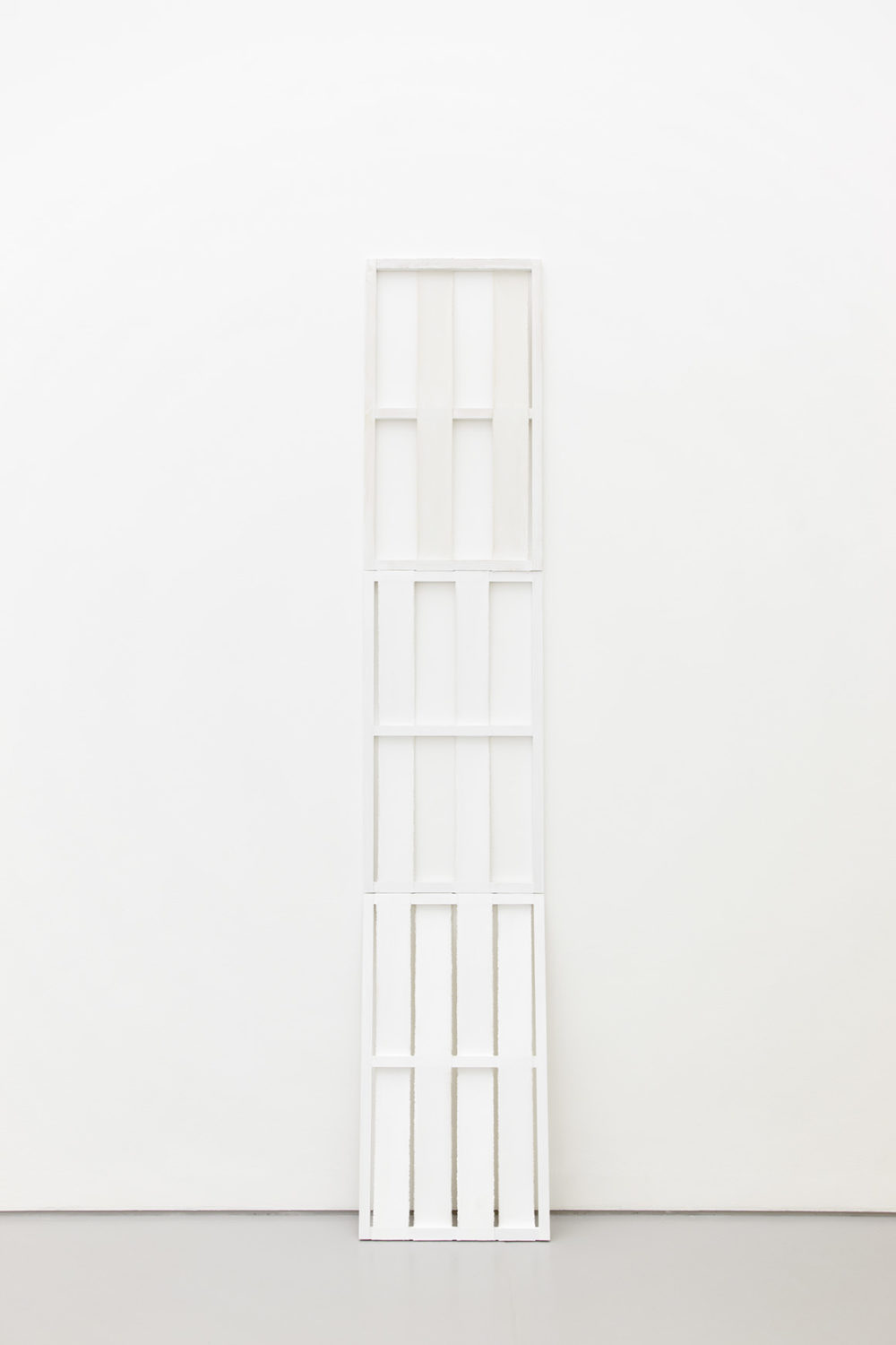 Installation view of Jessica Warboys Ab Ovo (2013). A geometric white wooden structure leans against a gallery wall.