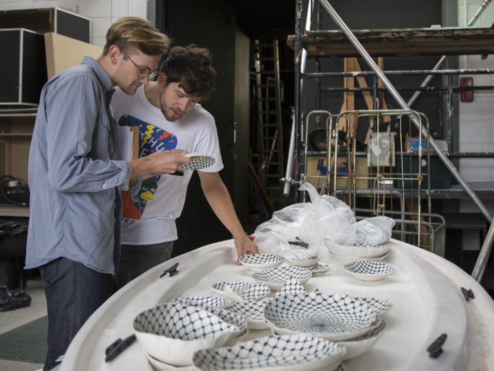 Production shot: Two men study porcelain bowls.
