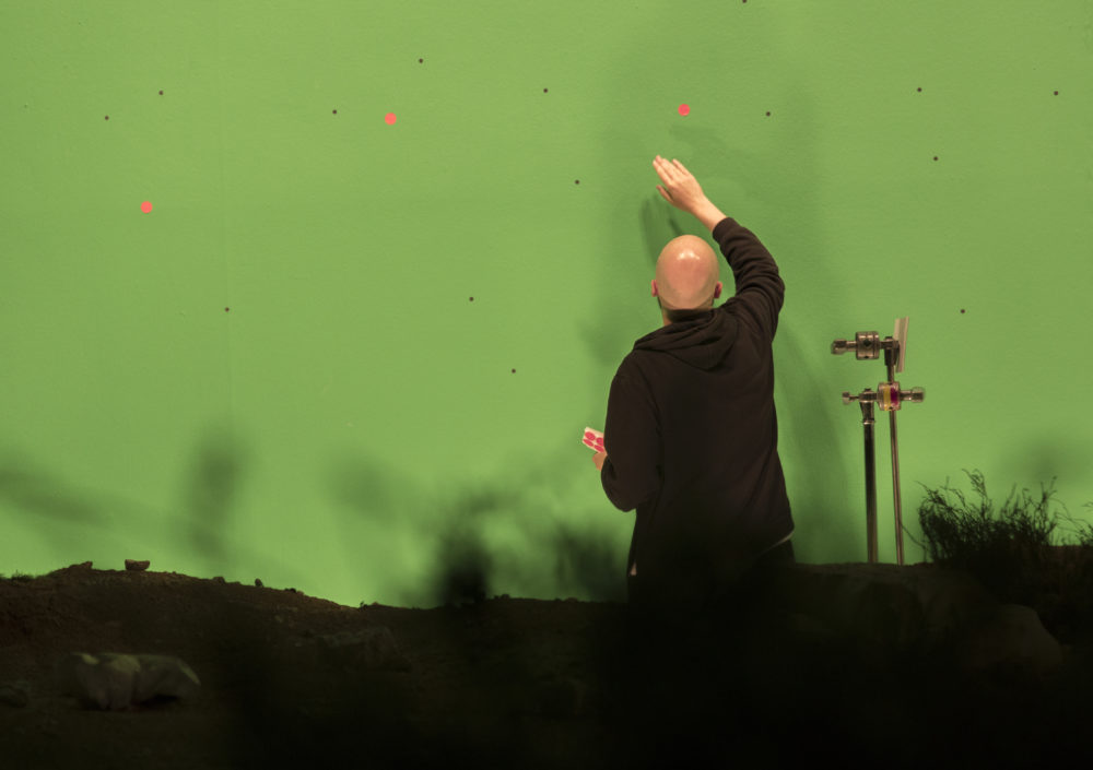 Production shot: A man tends to a green screen.