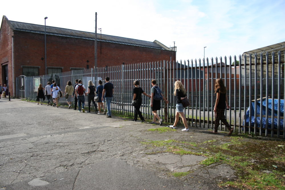 A group of people walk alongside an unfriendly metal fence.