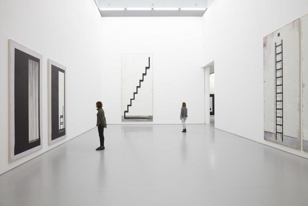 Two visitors study the large black and white paintings in the gallery.