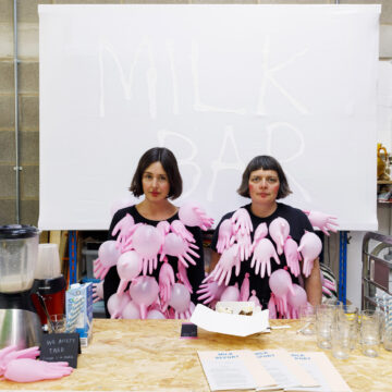 Two people sitting down with filled bright gloves attached to their bodies