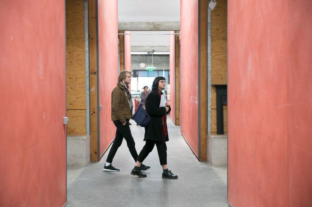 Two visitors walk between artist studios.