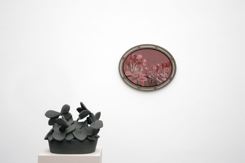 Installation view of Prophet (2008). A geometric sculpture made of clay sits on a plinth, a framed image of flowers hangs on the wall behind.