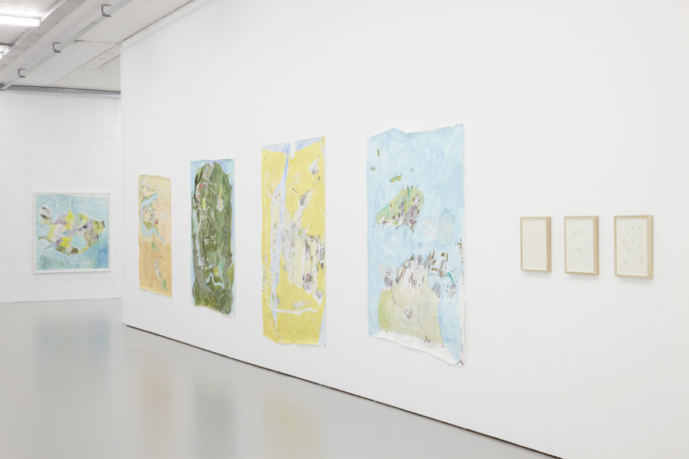 The white walls of the gallery are decorated with large pictures of maps in bright blue and green and yellow.