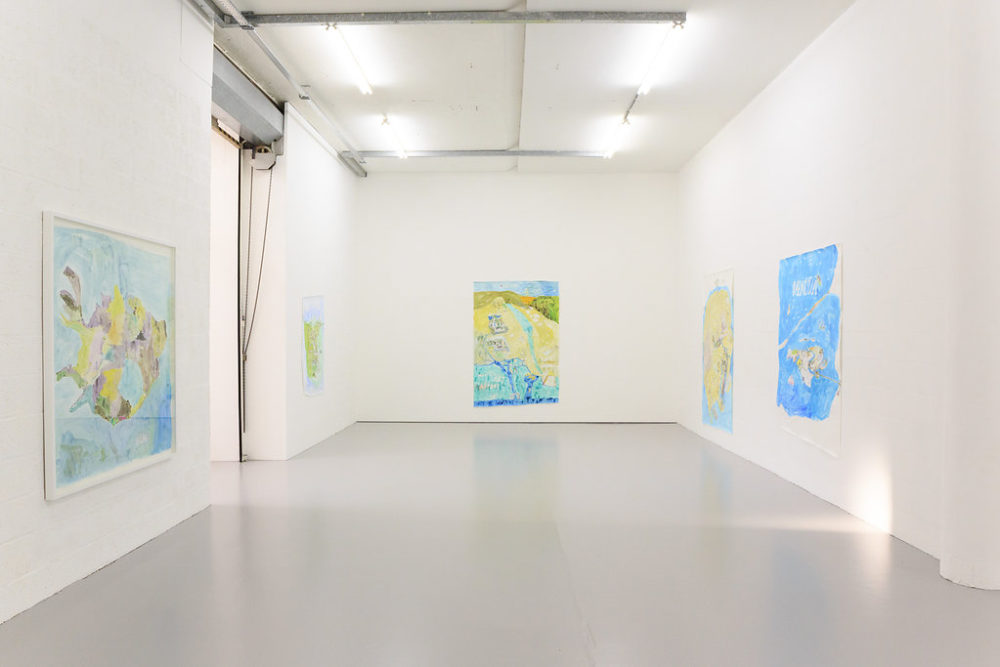 The white walls of the gallery are decorated with large pictures of maps in bright blue and green and yellow.