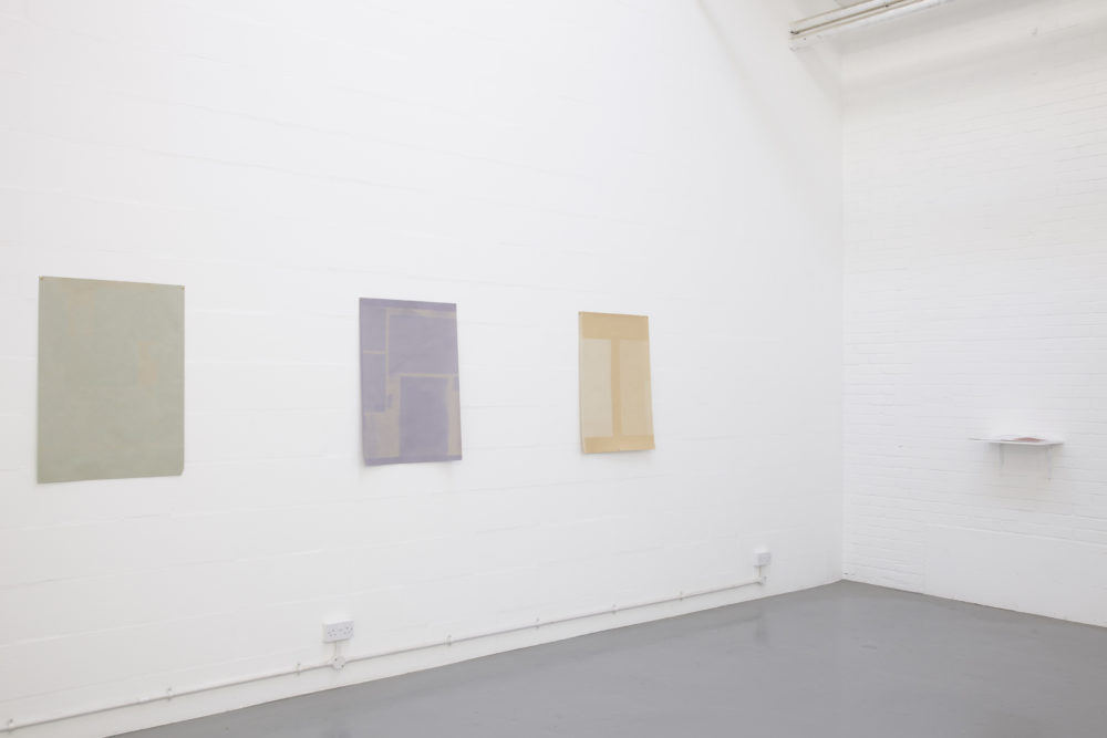 Installation view of Sara MacKillop, Faded Paper (2011). Three sheets of sugar paper, faded by the sun, are pinned to the white gallery wall.
