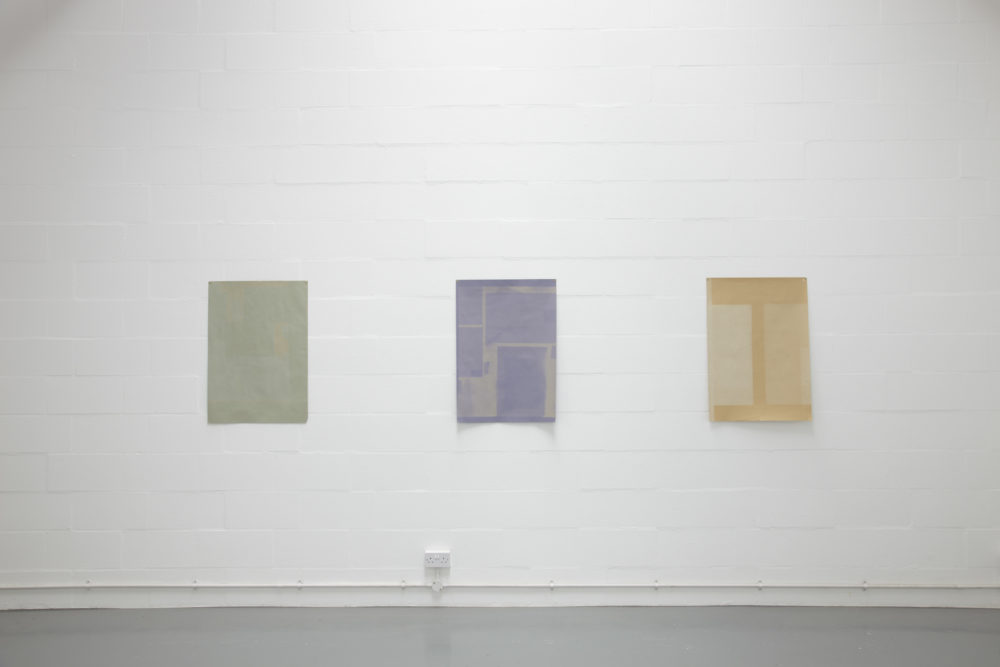 Installation view of Sara MacKillop, Faded Paper (2011). Three sheets of sugar paper, faded by the sun, are pinned to the white gallery wall.