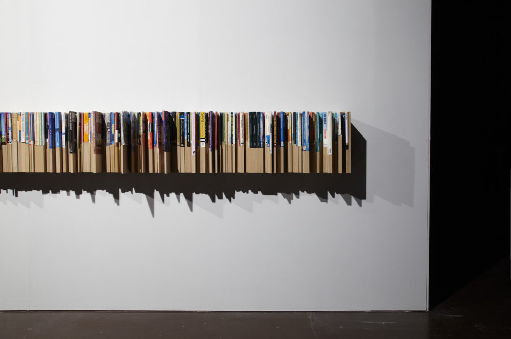 Installation view of Savage Presents Jean Michel Jarre (2011). An uneven bookshelf is made so that books of different heights all sit flush with one another.