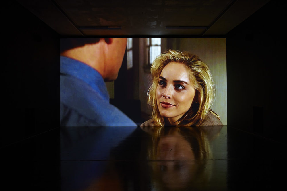 Installation view of Savage Presents Jean Michel Jarre (2011). A projection of a blonde woman smiling at a man in blue.