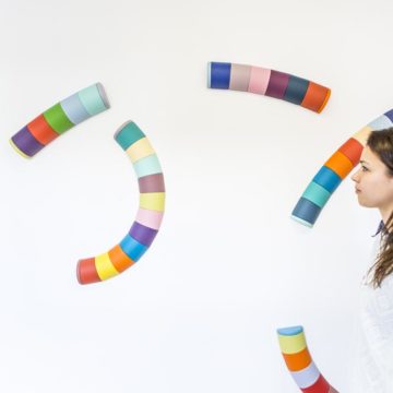 Colourful, curved tubes are suspended in air. A woman studies them.