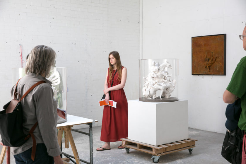 Three visitors look at sculptural work in an artists' studio.