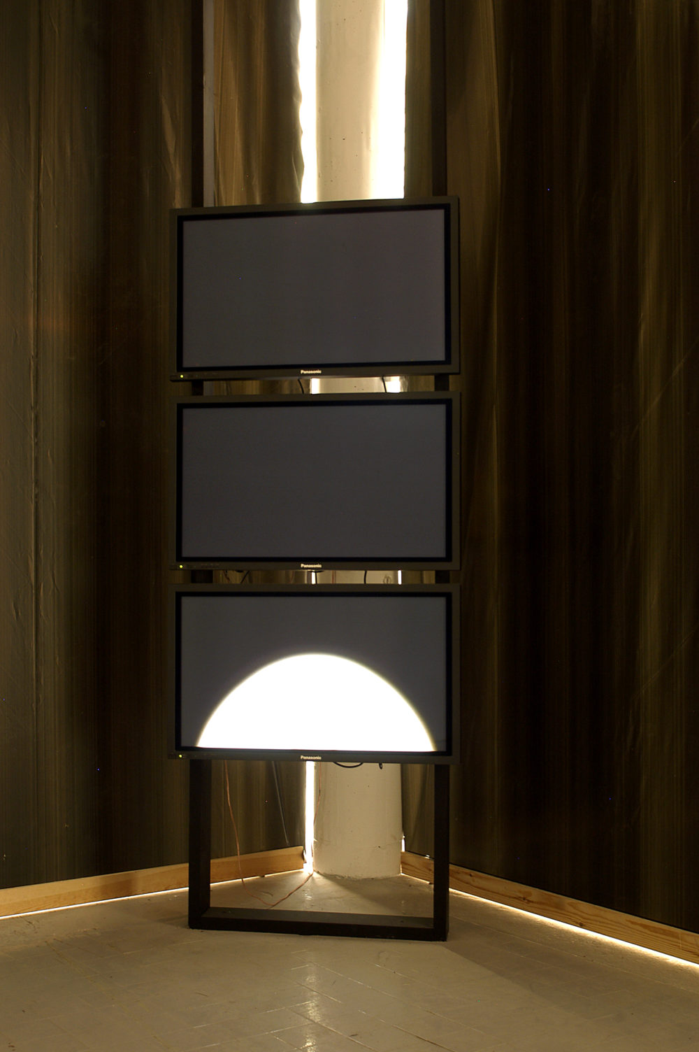 Installation view of Spin Cycle (2004). Three television screens are stacked atop one another. The bottom screen has a half circle of white rising from the bottom.