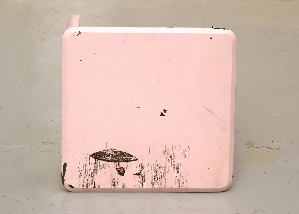 Installation view of Spin Cycle (2004). A wooden square stool that is painted baby pink lies on its side.