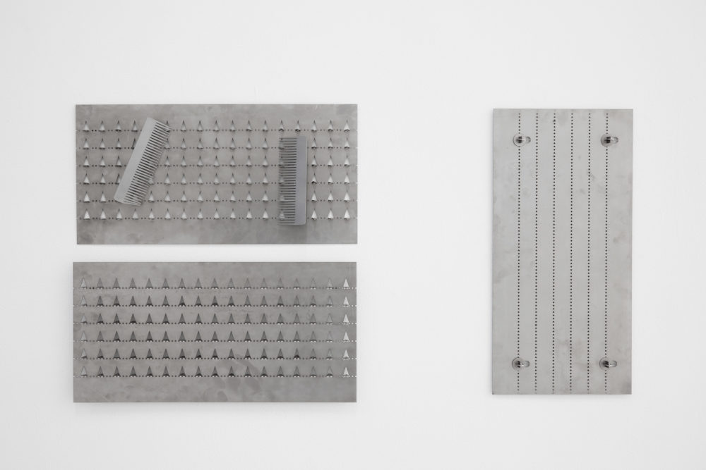 Metal sheets have been perforated and adapted to create structures. Three of these hang on white gallery walls.