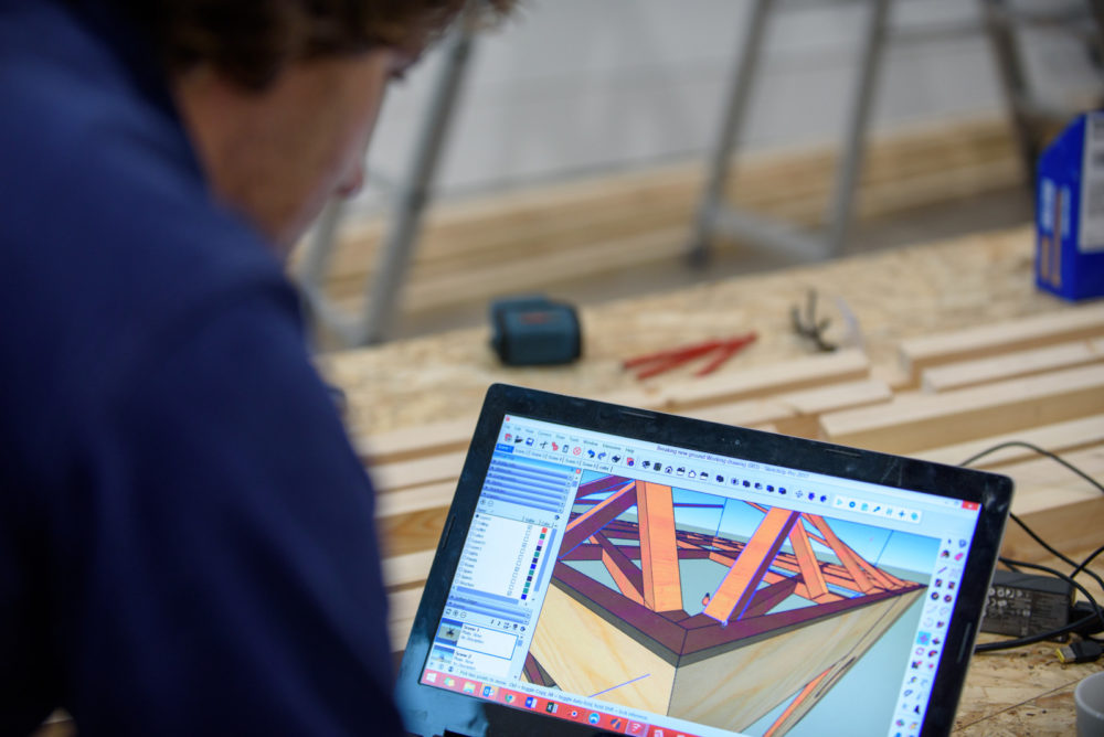 Installation shot: A technician studies a laptop with an image of the layout of a wooden structure.