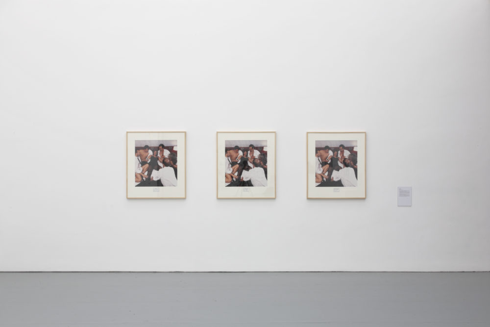 Installation view of Wealth of Nations (2010). The gallery is light and the walls are white. Three identical photographs of people hang on the walls.