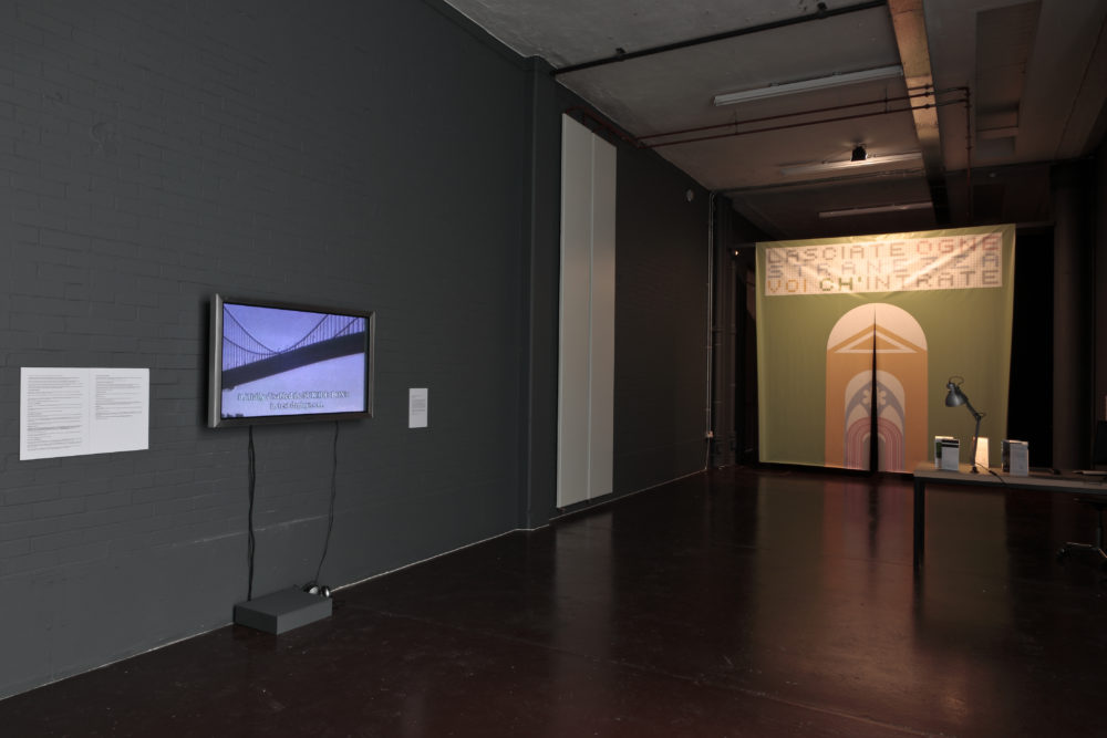 Installation view of Wealth of Nations (2010). The gallery is dim and the walls are painted in dark colours. A curtain with bold graphics is illuminated.