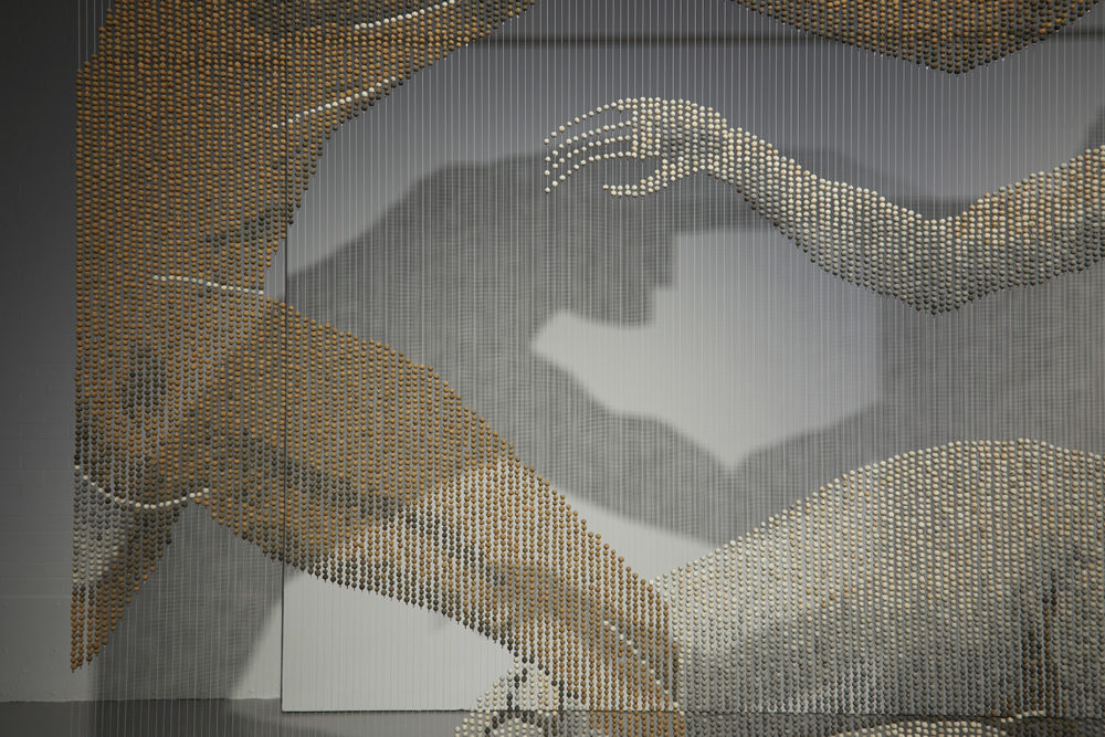 A close up of a bead curtain - the beads are depicting a series of nudes. In this close up you can see one nude's hip and another's hand.