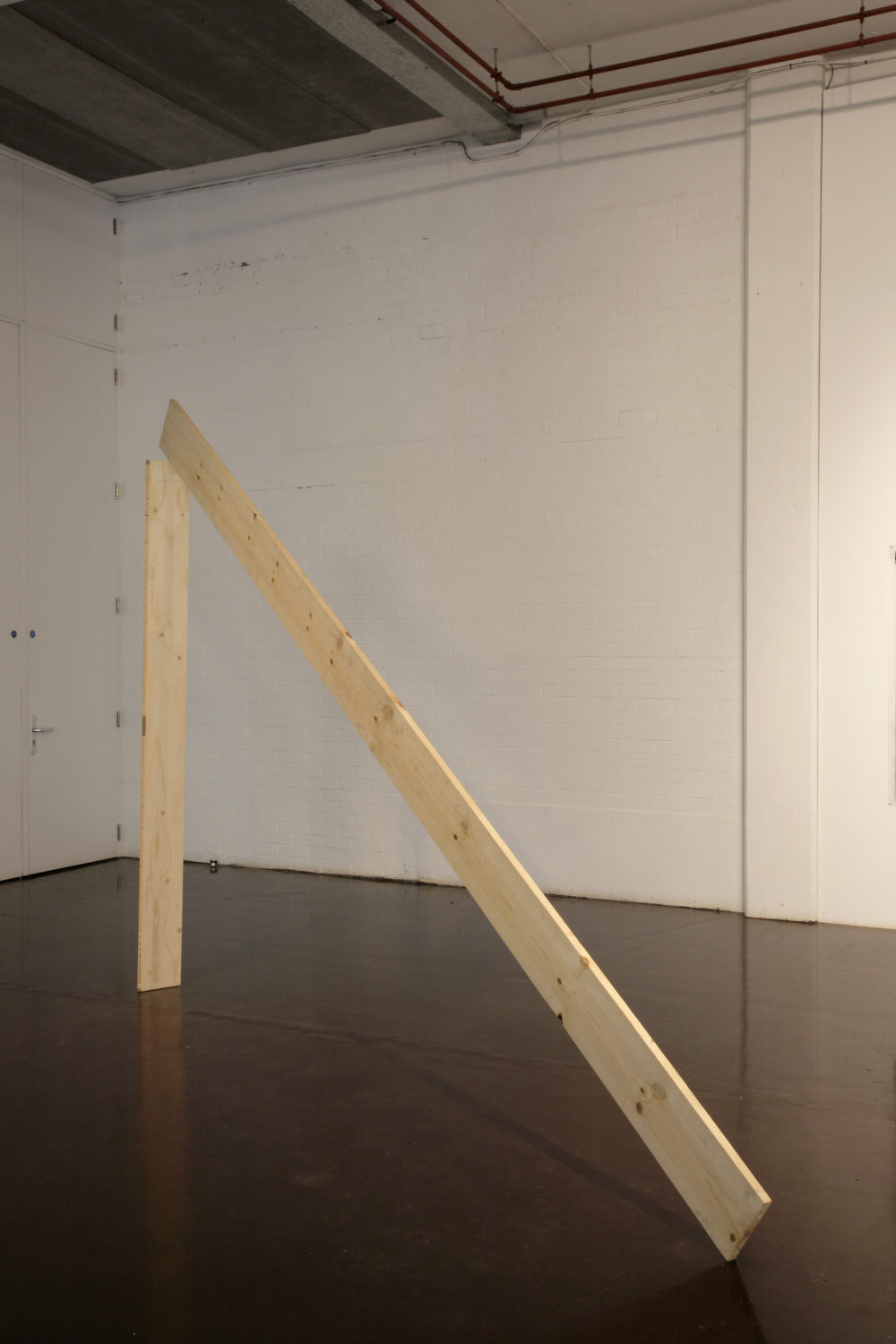 Installation view of Part-ilha, A River Ain't Too Much to Love (2011). A wooden plank stands vertically, and another leans against it.